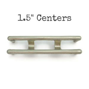 May include: A silver metal bracket with two holes, labeled "1.5" Centers".