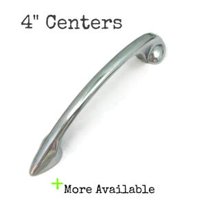 May include: A polished silver cabinet pull with a curved design. The text "4" Centers" is at the top, and "More Available" is at the bottom. The pull measures 4 inches (10.16 cm) between the centers of the mounting holes.