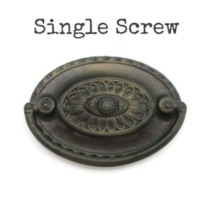 May include: An antique-style, oval drawer pull with a single screw mount. The bronze-colored hardware features an ornate, floral-inspired design in the center and on the edges. The text "Single Screw" is printed above the pull.