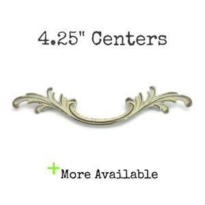 May include: An antique-style drawer pull with a curved design and ornate detailing. The pull is approximately 4.25 inches in length and has a distressed, off-white finish. Text on the image reads "4.25" Centers" and "More Available".