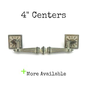 May include: Antique-style cabinet pull with a 4-inch (10.16 cm) center-to-center measurement. The pull features square backplates with a sunburst design and a decorative handle. The metal has a distressed, aged appearance. Text: 4" Centers, More Available.