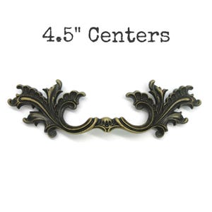 May include: An antique bronze-coloured drawer pull with ornate, scrolling leaf and floral designs. The text "4.5" Centers" is printed above the pull. The pull is designed for furniture and cabinetry. The measurement is approximately 11.4 cm.