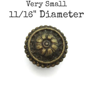 May include: A small, antique-style bronze button with a floral design in the center and a scalloped edge. The text "Very Small 11/16" Diameter" is printed above the button.