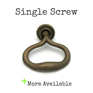 May include: Antique brass-toned drawer pull with a circular top and a curved handle. The text "Single Screw" is above the pull, and "More Available" is below it.