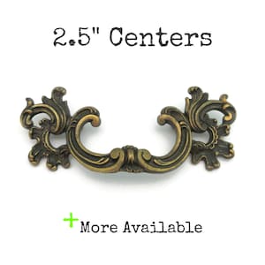 May include: Ornate bronze-toned drawer pull with a curved handle and decorative scrollwork. The text "2.5" Centers" is above the pull. The text "More Available" is below the pull.