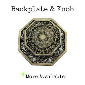 May include: An antique brass backplate and knob set. The octagonal backplate and knob feature intricate, ornate designs. The text "Backplate & Knob" is at the top, and "More Available" is at the bottom.