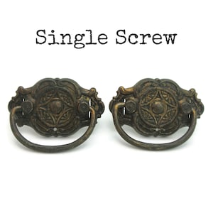 May include: Two antique bronze drawer pulls with ornate floral designs and a curved handle. The pulls have a distressed finish and are mounted with a single screw. The text "Single Screw" is above the pulls.