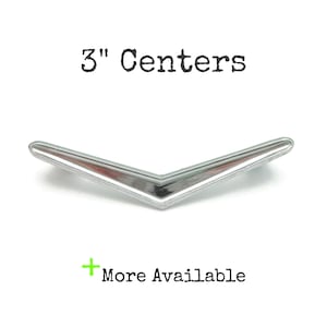 May include: A chrome-finished, V-shaped decorative hardware piece. The text "3" Centers" is above the hardware, and "More Available" is below. The hardware measures 3 inches across.
