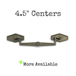 May include: A bronze-toned metal drawer pull with a drop handle and two hexagonal mounting plates. The text 4.5" Centers is printed above the hardware, and a green plus sign with the text More Available is printed below the hardware.