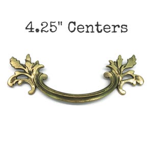 May include: A brass-toned metal drawer pull with a curved handle and ornate leaf-shaped ends. The text 4.25" Centers is printed above the hardware, indicating the distance between the mounting points for this piece of furniture hardware.