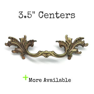 May include: An antique-style brass drawer pull with a decorative floral design. The pull has a measurement of 8.89 cm between the centres of the mounting holes. The text "3.5" Centers" is above the pull, and "More Available" is below.