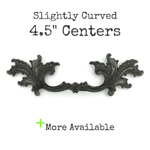 May include: Ornate, dark bronze-colored cabinet pull with a curved design. The pull has a 4.5-inch center-to-center measurement and features decorative floral and scrollwork details. The text "Slightly Curved 4.5" Centers" is above the pull.