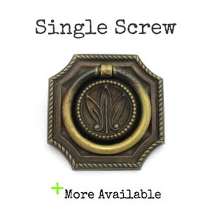 May include: Antique brass-toned drawer pull with a ring handle. The pull has a decorative floral design in the center and a rope-like border. The text "Single Screw" is above the pull, and "More Available" is below.