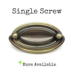May include: Oval-shaped antique brass drawer pull with a dark bronze center and two round knobs. The text "Single Screw" is above the pull, and "More Available" is below.