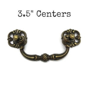 May include: A brass-toned metal drawer pull with a curved handle and two ornate, circular mounting plates. The hardware features a dark, aged finish with intricate detailing. The text 3.5" Centers is printed above the drawer pull.