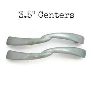 May include: Two silver-toned cabinet pulls with a twisted design. The pulls are 3.5 inches apart.