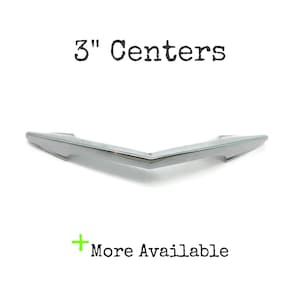 May include: A polished chrome cabinet pull with a V-shaped, angular design. The text 3" Centers is printed above the hardware, and the text + More Available is printed below the hardware, indicating the distance between the mounting points.