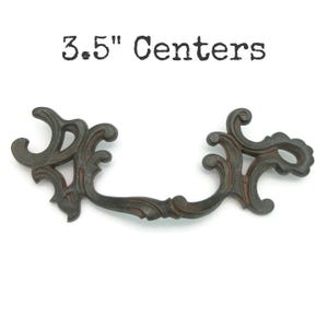 May include: Ornate, dark bronze-colored drawer pull with a decorative scroll design. The text "3.5" Centers" is printed above the pull. The pull is designed for a 3.5-inch center-to-center installation.