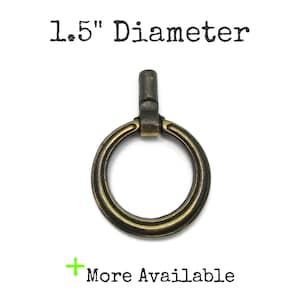 May include: A brass-toned metal ring pull with a weathered finish and a vertical mounting post. The text 1.5" Diameter is printed above the object, and the text + More Available is printed below the object on a plain white background.