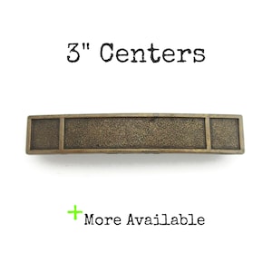 May include: A rectangular bronze-colored cabinet pull with a textured center section and two end sections. The text "3" Centers" is above the pull, and "More Available" is below it.