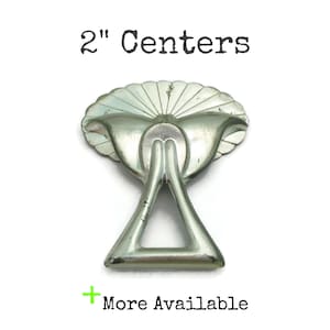 May include: Silver-toned metal drawer pull with a decorative fan-shaped design. The pull has a 2-inch center-to-center measurement. "2" Centers" is printed on the white background.