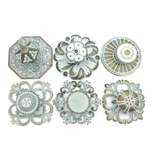 May include: Six decorative cabinet knobs in various shapes and designs. The knobs feature distressed white, gold, and silver finishes. Styles include floral, geometric, and ornate patterns, suitable for furniture or home decor projects.