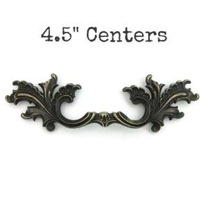 May include: An antique bronze-colored drawer pull with ornate, symmetrical floral detailing. The text "4.5" Centers" is printed above the pull. The pull is approximately 4.5 inches in length, suitable for furniture restoration or decorative projects.