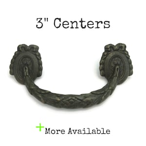 May include: Antique bronze drawer pull with a decorative floral design. The pull has a 3-inch (7.6 cm) center-to-center measurement. The text "3" Centers" is above the pull, and "More Available" is below.