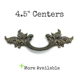 May include: A bronze-toned metal drawer pull with an ornate, scrolling leaf design and a curved handle. The text 4.5" Centers is printed above the hardware, and the text + More Available is printed below the hardware in black and green.