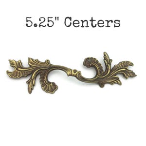 May include: Ornate antique brass drawer pull with a scrolling leaf design. The pull measures 5.25 inches between the screw centers. The text "5.25" Centers" is printed above the pull.