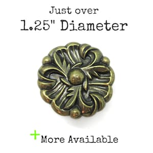 May include: Ornate, antique brass-colored decorative button with a floral design. The button is just over 1.25" in diameter. The text "Just over 1.25" Diameter" and "More Available" are also visible.