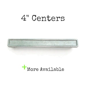 May include: A silver metal drawer pull with a 4" center to center measurement. The pull is rectangular with a slightly textured surface.
