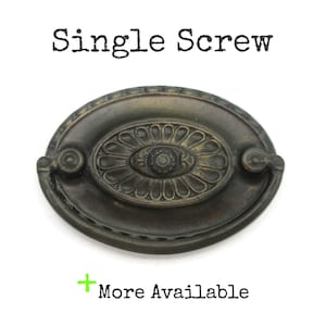 May include: An antique bronze-toned drawer pull with an oval shape and ornate floral design. The center features a detailed rosette, and the text "Single Screw" is above the pull. The text "More Available" is below the pull.