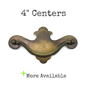 May include: A brass-toned metal drawer pull with a curved handle and a decorative backplate. The text 4" Centers is printed above the pull, and the text + More Available is printed below the pull on a plain white background.