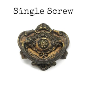 May include: Ornate antique brass drawer pull with a decorative design. The pull features a central circular element and a curved handle. The text "Single Screw" is above the pull.