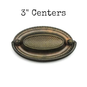 May include: Oval antique bronze drawer pull with a textured centre and rope-like edging. The pull has a 7.6 cm centre-to-centre measurement. The text "3" Centers" is above the pull.