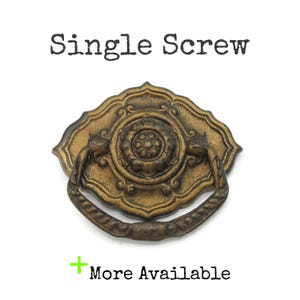 May include: Ornate antique brass drawer pull with a decorative floral center and a curved handle. The text "Single Screw" is above the pull, and "More Available" is below.