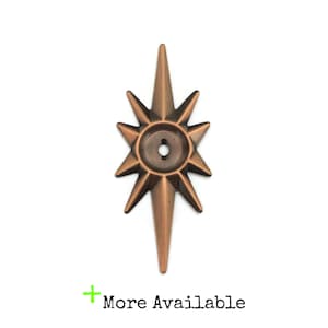 May include: A copper-coloured starburst-shaped metal knob with a single hole in the centre. The knob has a pointed tip and a starburst design with 12 points.
