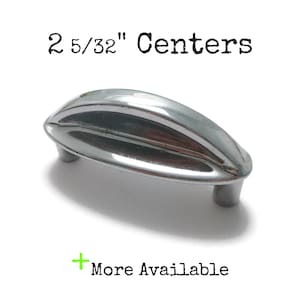 May include: A shiny, chrome-finished cabinet pull with a ribbed design. The text "2 5/32" Centers" is printed above the pull. The words "More Available" are printed below the pull.