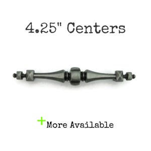 May include: A dark gray cabinet pull with a decorative design. The pull measures 4.25 inches between the centers of the mounting holes. The text "4.25" Centers" is above the pull, and "More Available" is below.