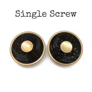 May include: Two round, black and gold screws with a central gold dot. The screws have a speckled texture and a gold rim. The text "Single Screw" is above the screws.