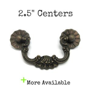 May include: Antique bronze drawer pull with a decorative shell and floral design. The pull has a 2.5-inch center-to-center measurement. The text "2.5" Centers" is above the pull, and "More Available" is below.