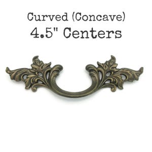 May include: Antique bronze-colored drawer pull with a curved, concave design. The pull features ornate, leaf-like detailing on each end and a curved handle. Text on the image reads "Curved (Concave) 4.5" Centers."
