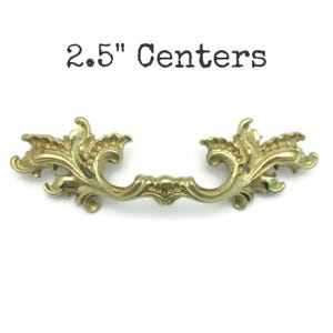 May include: Ornate brass drawer pull with a floral design. The pull has a 2.5-inch center-to-center measurement. The text "2.5" Centers" is printed above the pull.