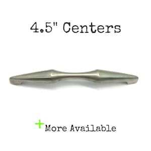 May include: A silver-toned metal cabinet pull with a tapered, spindle-like shape. The text 4.5" Centers is printed above the handle, and the text + More Available is printed below the handle, indicating the mounting distance between the screws.