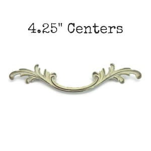May include: An antique-style drawer pull with a curved design and ornate leaf details. The text "4.25" Centers" is above the pull. The pull is a light, aged color, suggesting a vintage aesthetic.