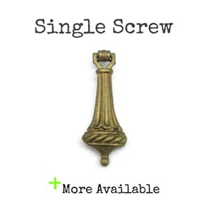 May include: A brass-toned metal drop pull with a vertical fluted design and a twisted rope detail at the base. The object features a hinged top loop for mounting. Text above reads Single Screw and text below reads More Available.