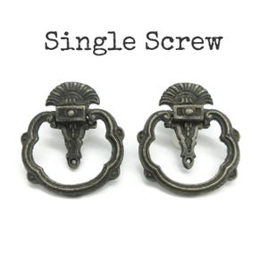 May include: Two antique-style metal drawer pulls with a dark, weathered finish. Each pull features a decorative fan-shaped top, a central vertical mount, and a circular drop handle. The text "Single Screw" is printed above the hardware.