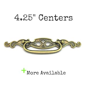May include: Antique brass-finished drawer pull with a decorative design. The pull has a handle and measures 4.25 inches between the mounting holes. The text "4.25" Centers" is above the pull, and "More Available" is below.