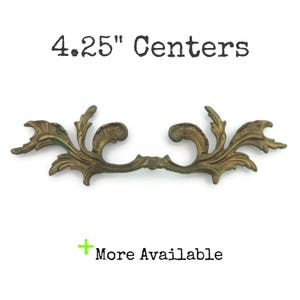 May include: An antique-style cabinet pull in a bronze finish, featuring an elaborate floral pattern. The pull has a measurement of 10.8 cm between the centres. The text "4.25" Centers" is above the pull, and "More Available" is below.